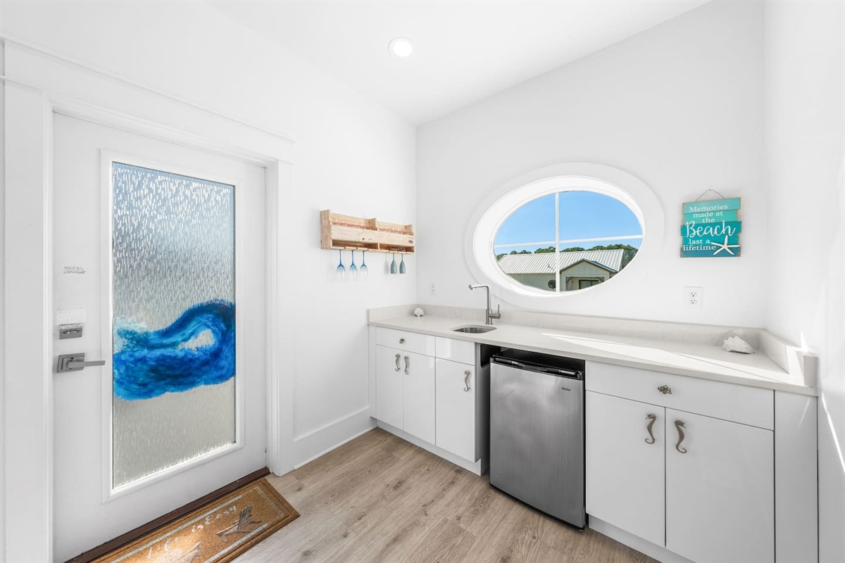 3rd-floor wet bar with a fridge, glass rack, and nautical Quatrefoil windows. ⚓️ Kids and adults love the  seahorse handles!  Grab a drink and head to the deck for a movie night on the outdoor projector. The ultimate family hangout!