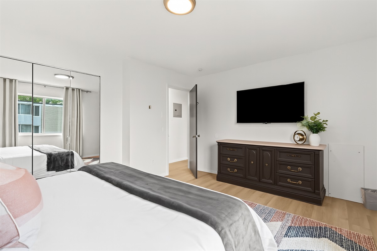 Spacious bedroom with Smart TV, dresser, and plenty of natural light for your comfort.