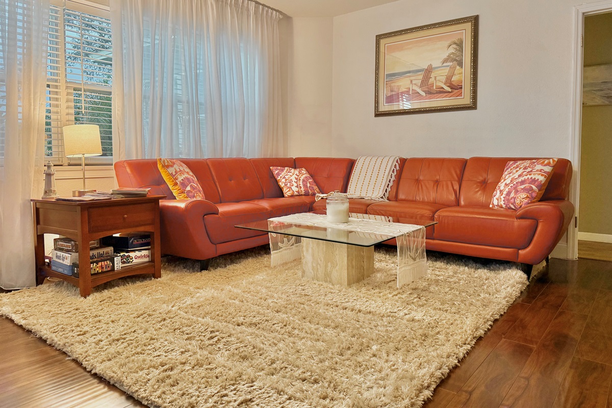Kick back on the plush leather sectional surrounded by soft textures, coastal art, and natural light streaming through sheer curtains.