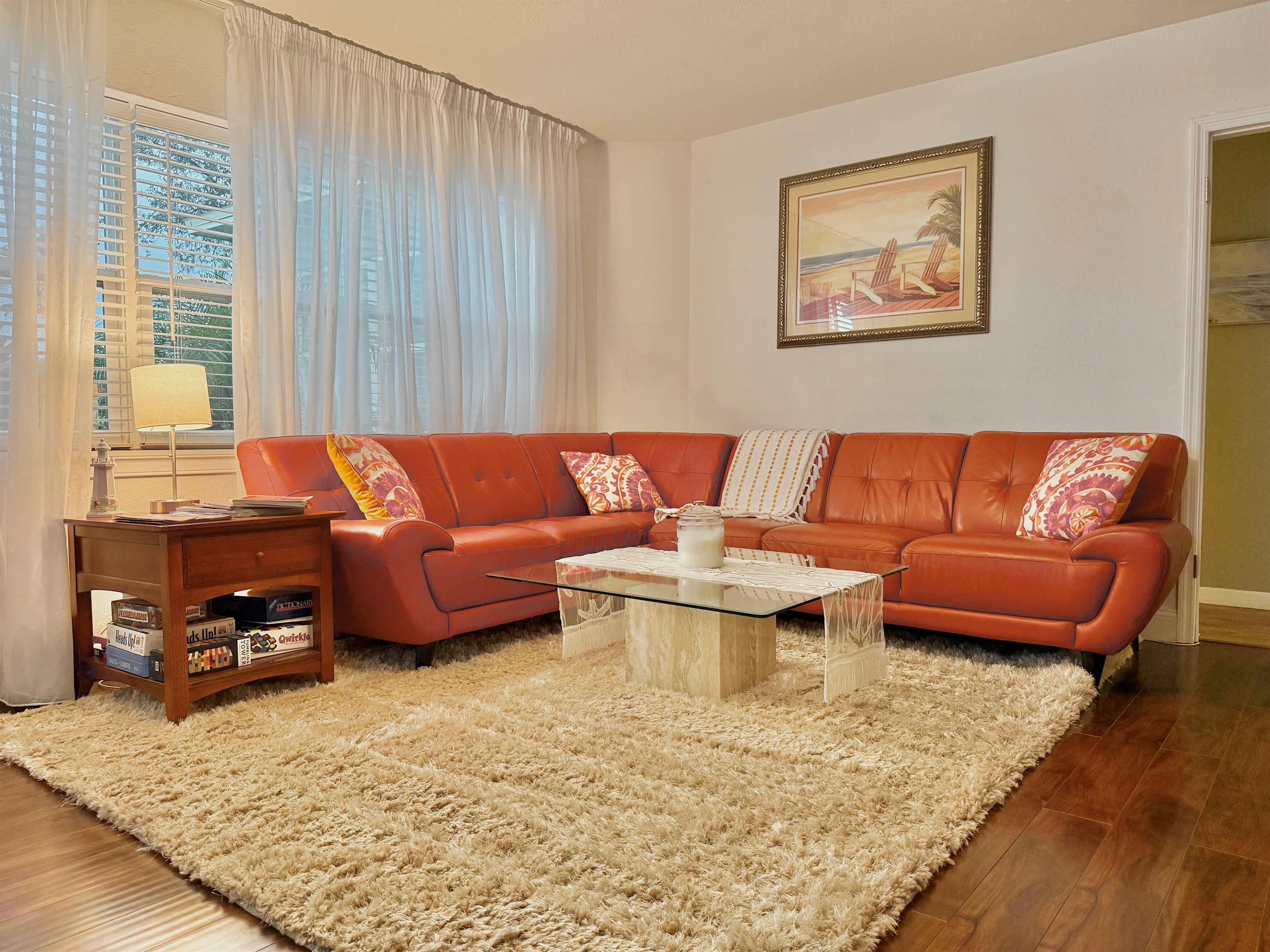 Kick back on the plush leather sectional surrounded by soft textures, coastal art, and natural light streaming through sheer curtains.