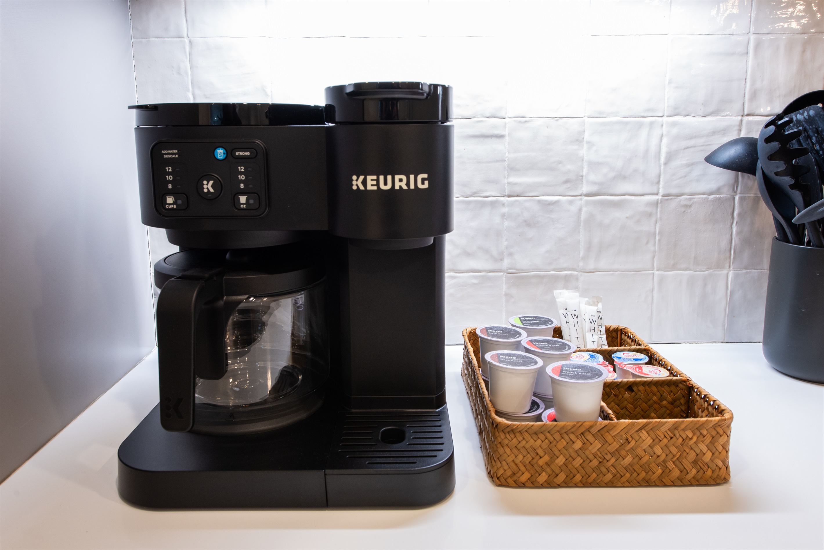 Keurig Coffee Station: A sleek Keurig coffee maker sits ready for use, accompanied by a wicker basket filled with an assortment of K-cups and sugar packets, ensuring a perfect cup of coffee is just a button press away.