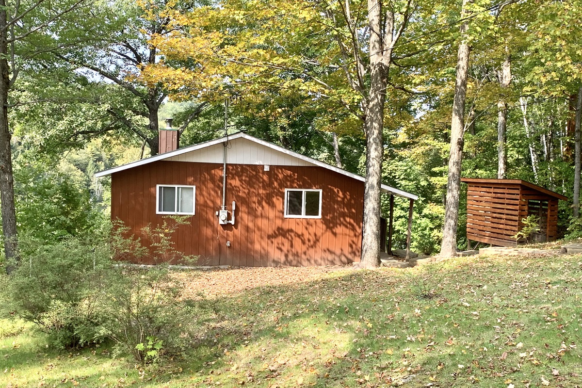 Cottage frontal view, fully under tall mature sugar maple trees