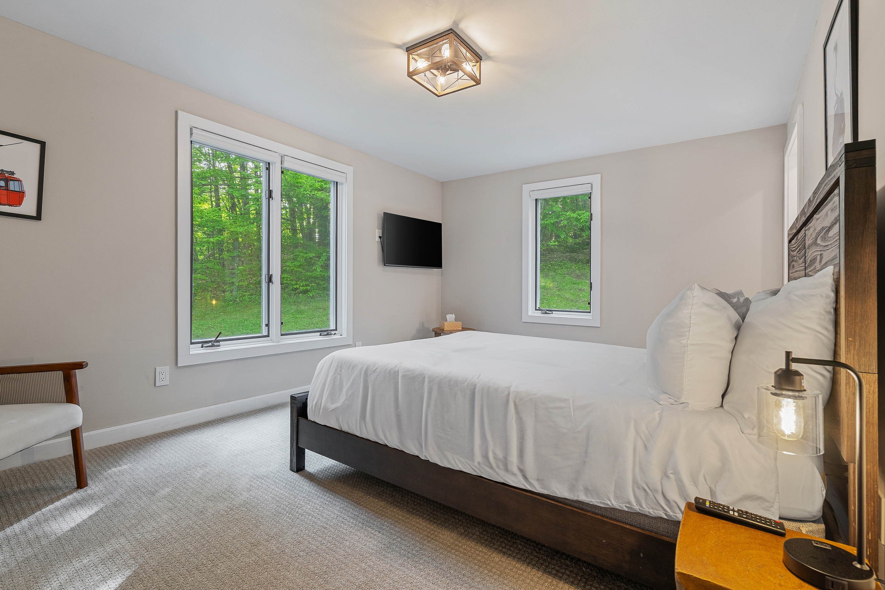 Bedroom with queen bed, flat-screen TV and windows framing the surrounding forest