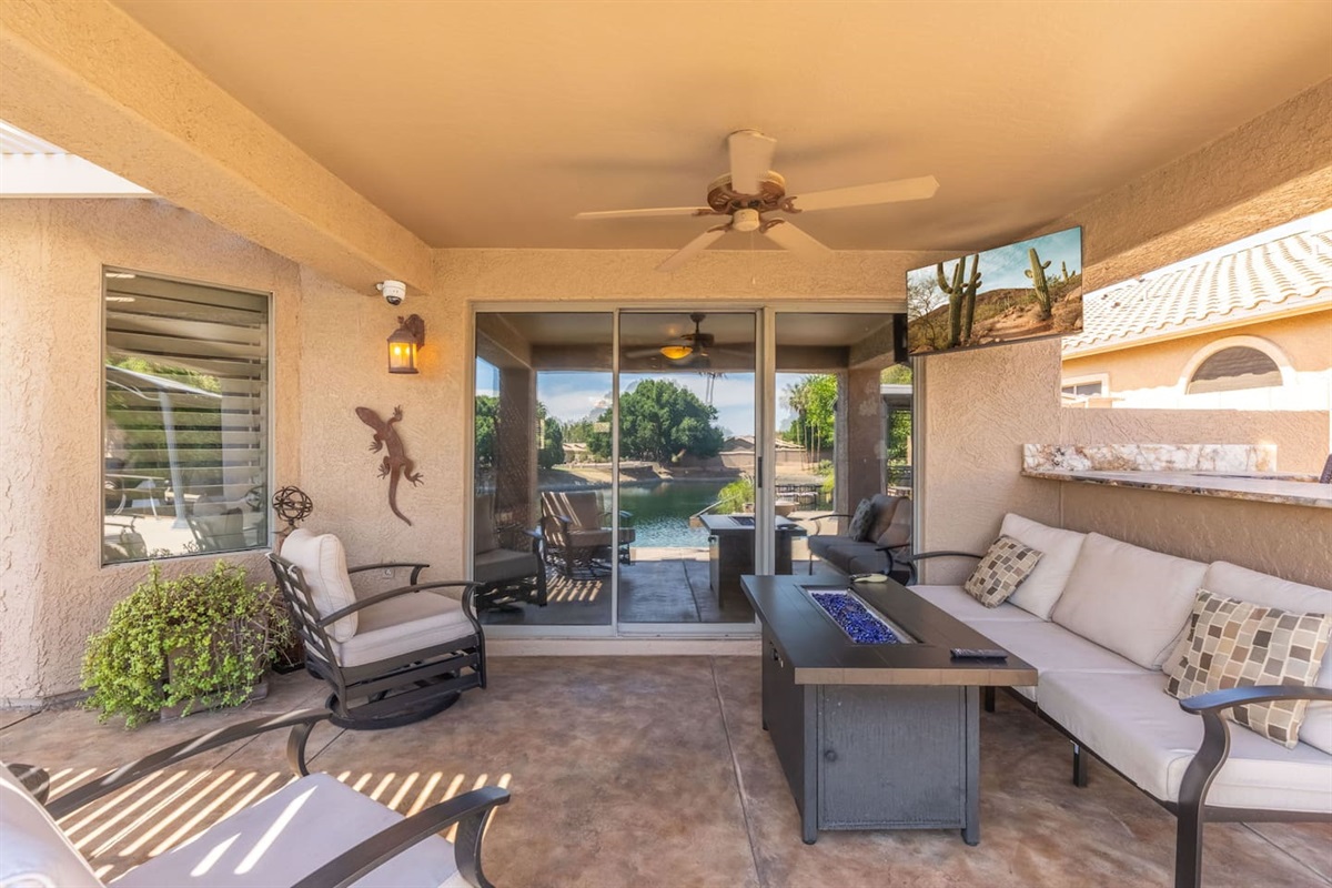 The covered patio seamlessly connects indoor and outdoor living — step through the sliding glass doors from the living room and settle into the cushioned seating around the fire table.