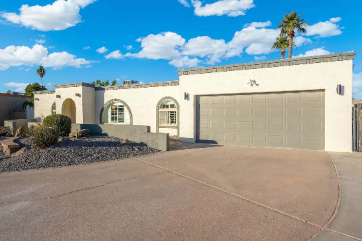 Classic Southwest architecture greets guests from the curb, with clean stucco lines, arched windows, and a spacious driveway that fits the whole group's cars with room to spare.