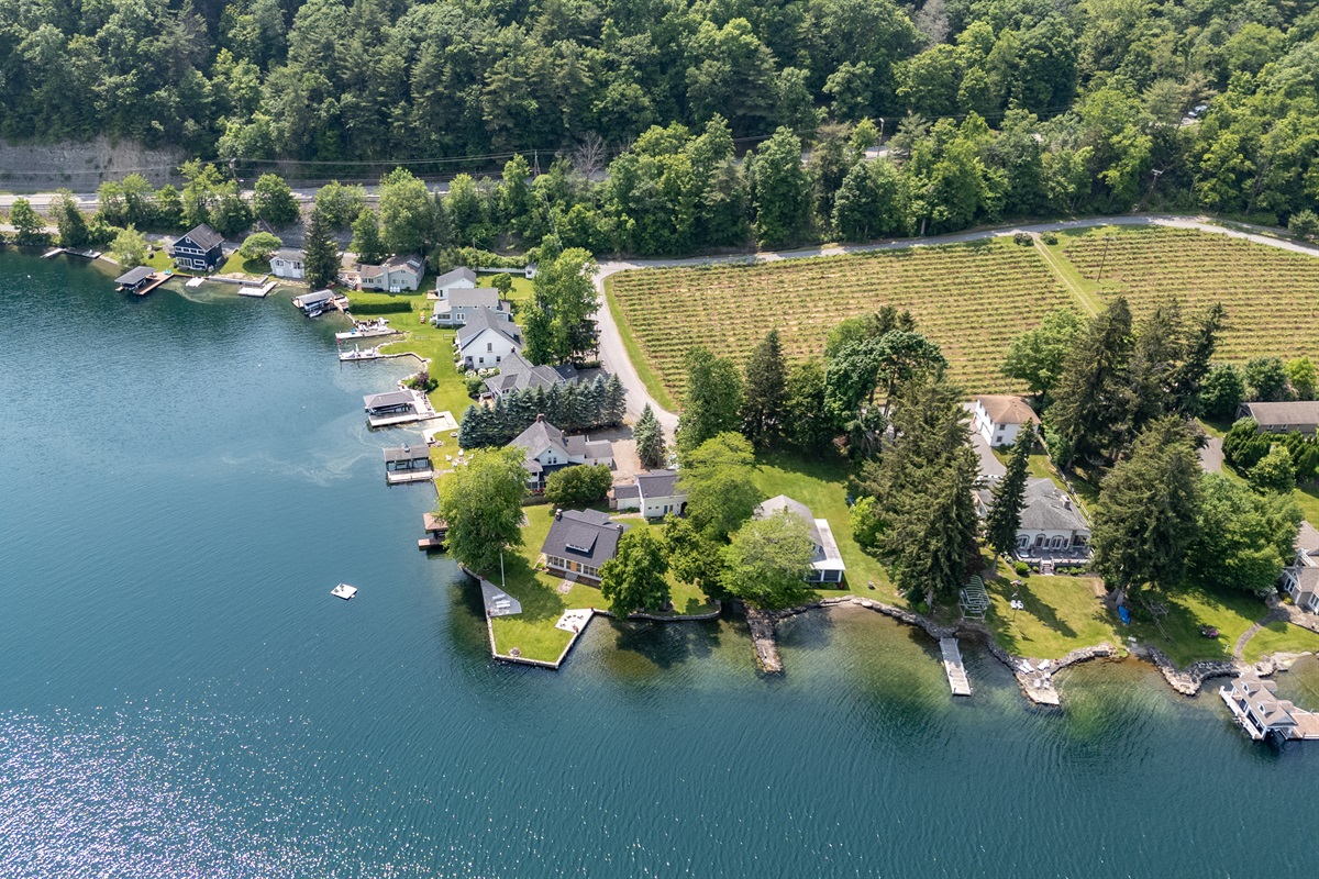 A stunning aerial view of lakeside living meets vineyard charm—private docks, waterfront homes, and lush grape rows create the perfect Finger Lakes retreat.
