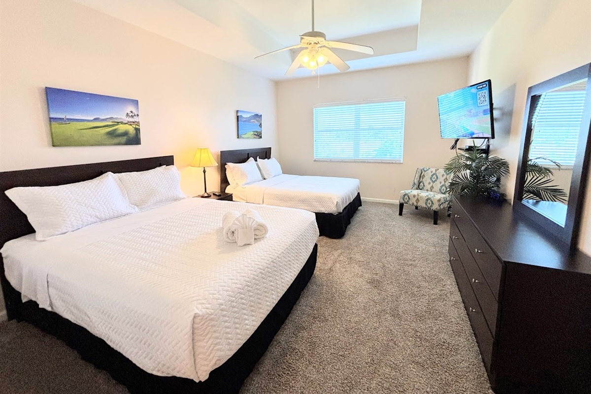 Comfortable bedroom with two beds, ceiling fan, TV, dresser storage, and natural light.