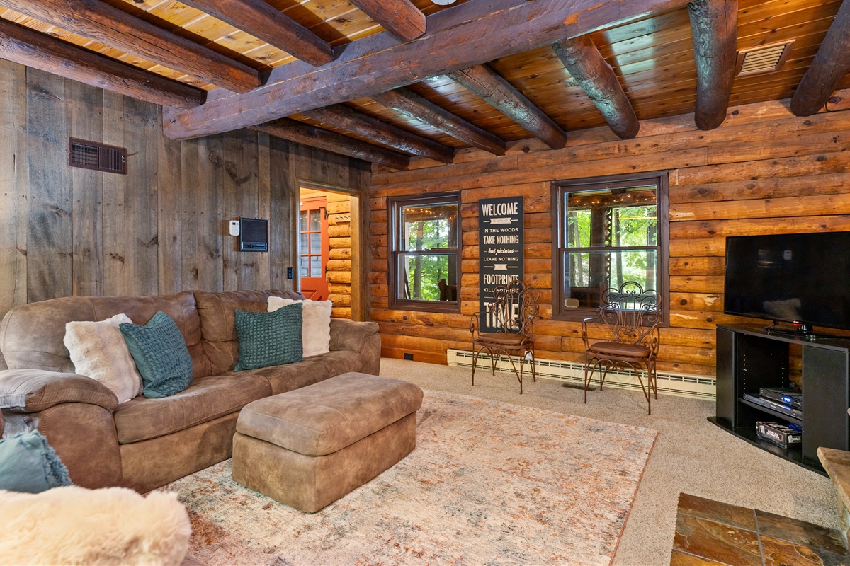 Charming log cabin living room featuring exposed beams, a grand stone fireplace, and plush seating for ultimate relaxation.