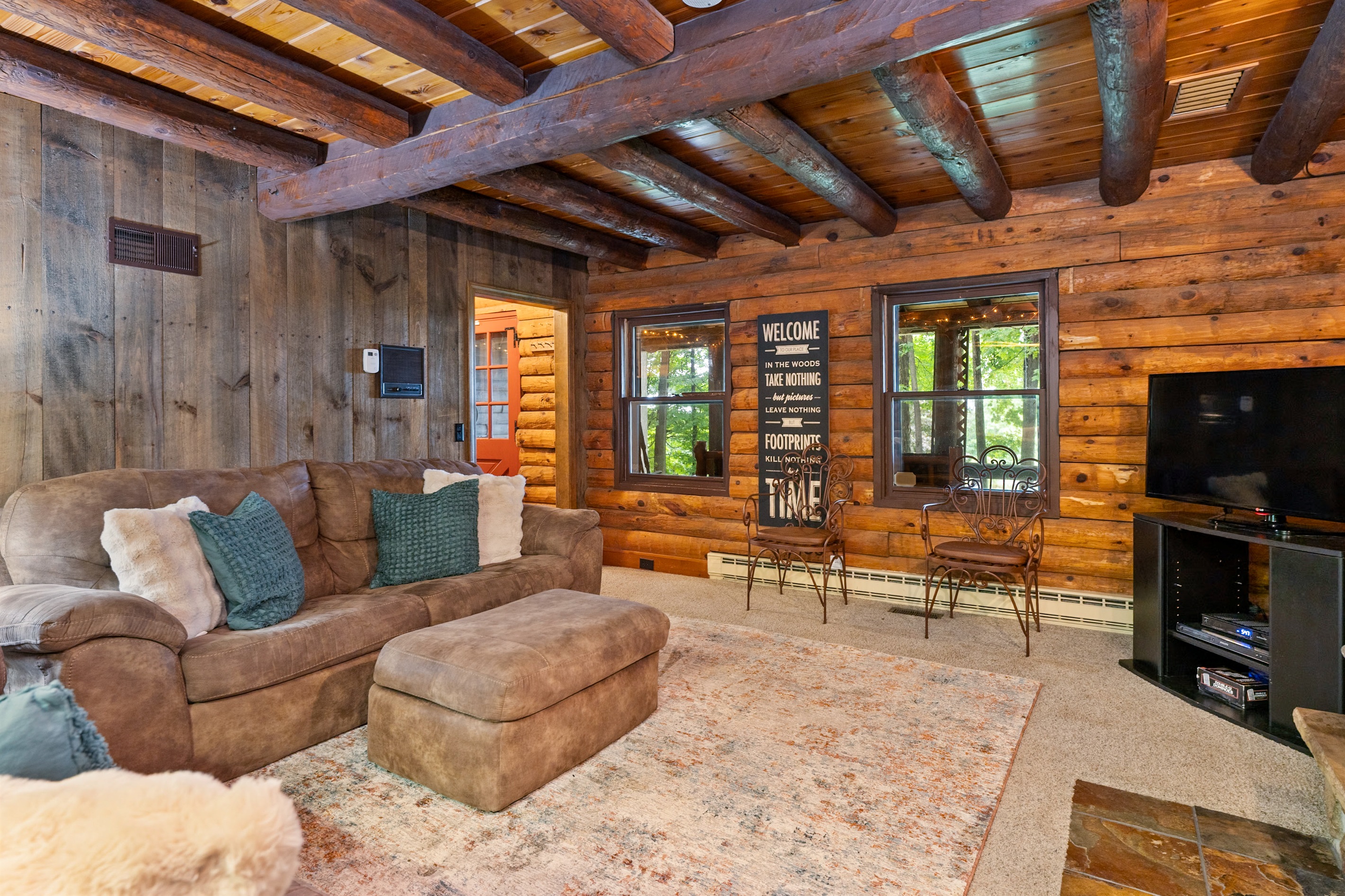 Charming log cabin living room featuring exposed beams, a grand stone fireplace, and plush seating for ultimate relaxation.