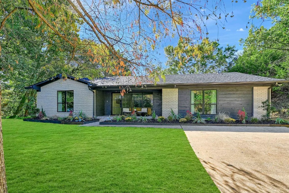 Front exterior view showcasing the modern ranch-style home, landscaped yard, and welcoming curb appeal surrounded by mature trees.