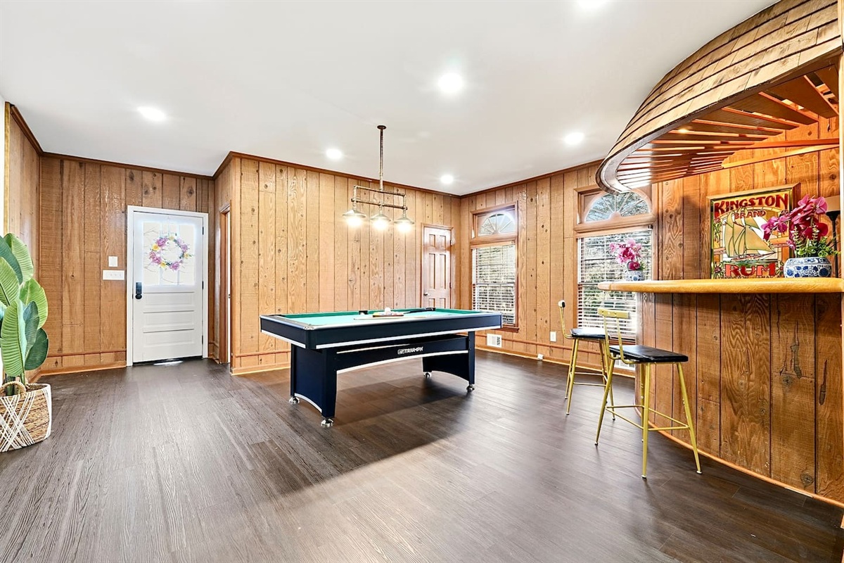 Enjoy this main-floor game room near the side entrance featuring a convertible pool and ping-pong table, a custom curved wood bar, and a Roku powered smart TV—ideal for entertaining and casual gatherings.