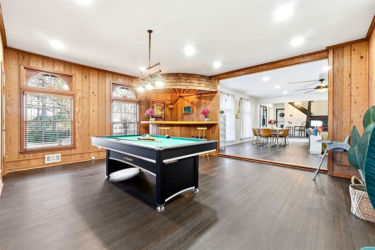 Enjoy this main-floor game room near the side entrance featuring a convertible pool and ping-pong table, a custom curved wood bar, and a Roku powered smart TV—ideal for entertaining and casual gatherings.