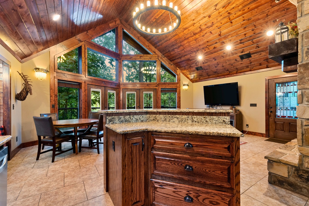 Open-concept kitchen and dining with vaulted ceilings and woodland views.
