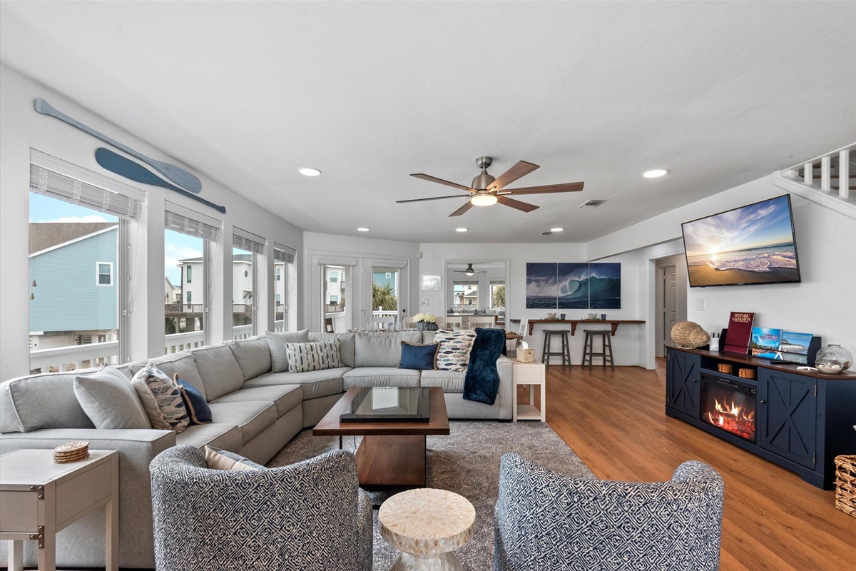 The living room features plenty of seating with a large, plush sectional couch, along with swivel chairs, wrapped in the ambiance of an electric fireplace and large screen TV. 