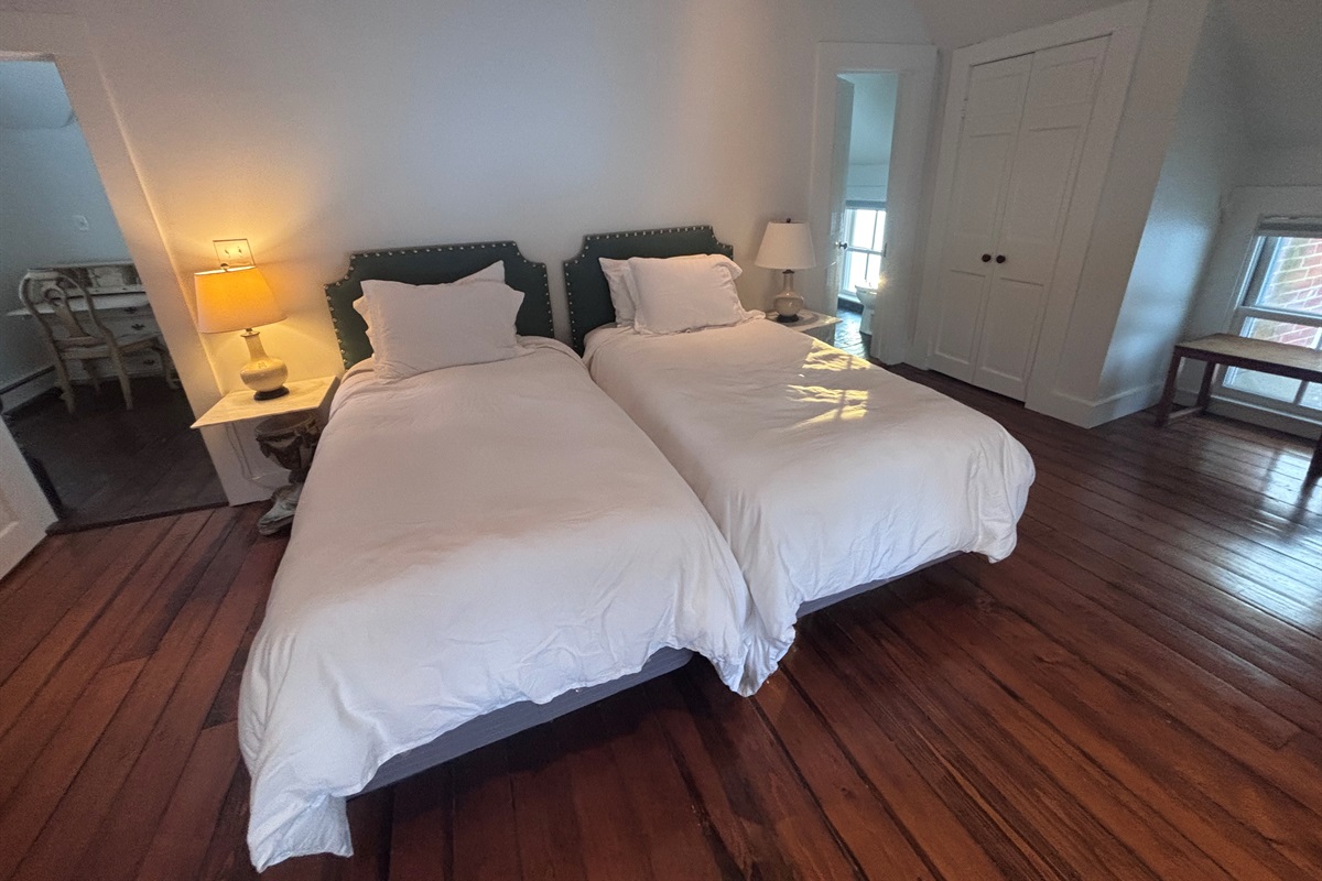 Bright guest bedroom with twin beds, hardwood floors, and soft natural light.