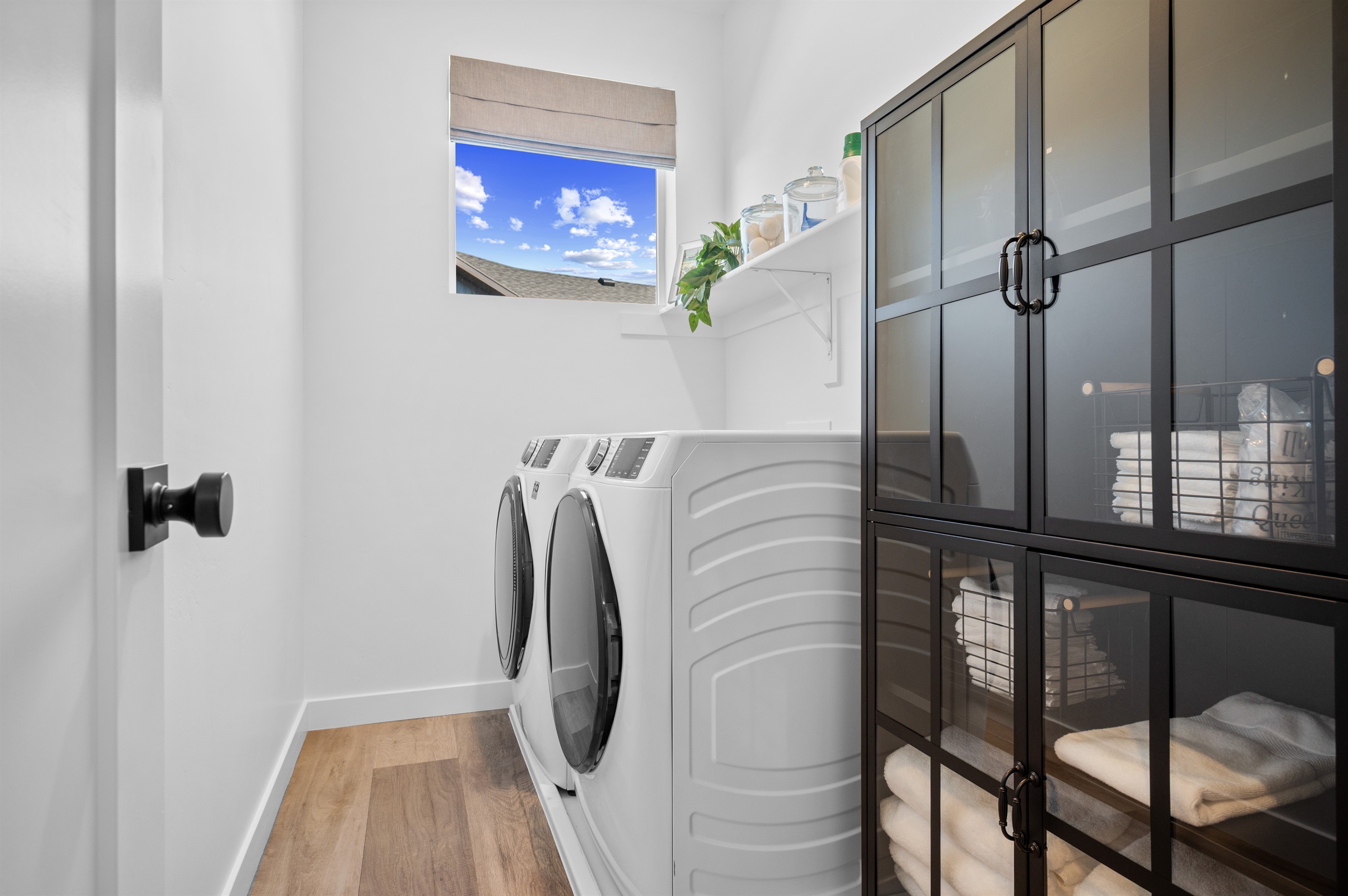 Convenient laundry room with modern washer and dryer, storage cabinet, and stocked shelves.