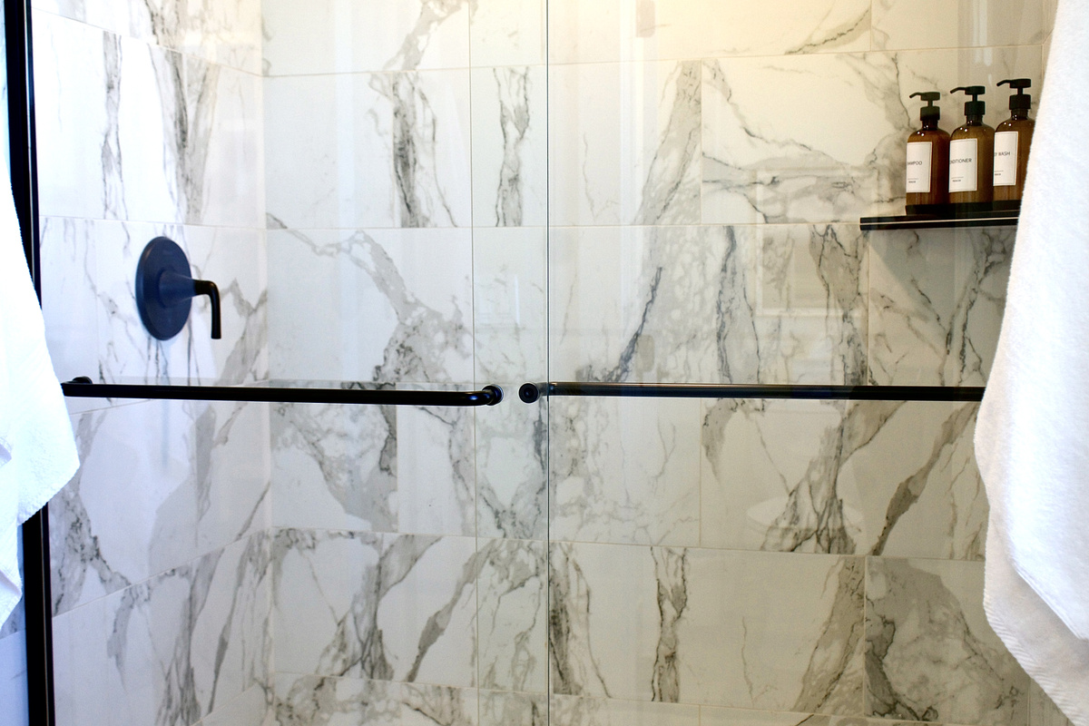 Large walk-in marble shower featuring a rainfall showerhead, offering a spa-like experience with a modern, luxurious finish.