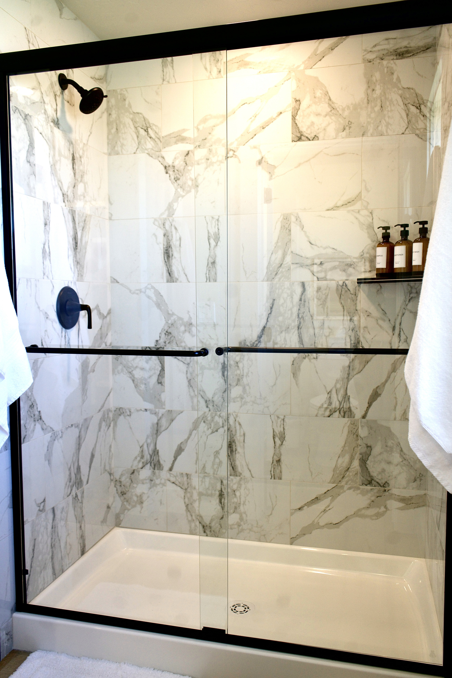 Large walk-in marble shower featuring a rainfall showerhead, offering a spa-like experience with a modern, luxurious finish.