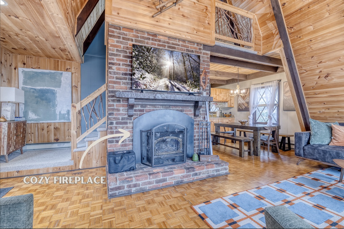 This inviting space features a brick fireplace and flat-screen TV. The high, angled ceilings and rustic wooden beams add cabin-like charm.