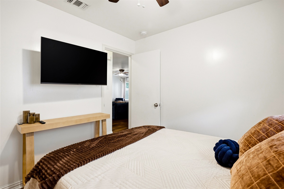 Double bedroom with velvet bedding, chest of drawers, ceiling fan, natural light, and Smart TV. Warm, well-decorated space with nightstands and closet — private and restful for couples or solo travelers.