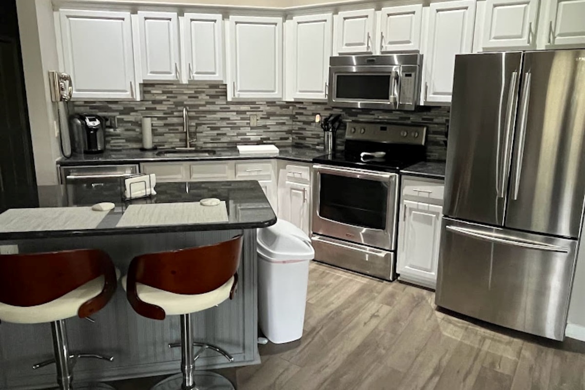 Updated kitchen featuring stainless steel appliances, white cabinetry, tile backsplash, breakfast bar seating, and wood-look flooring.