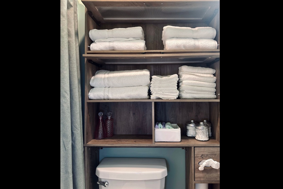 Hall bathroom storage featuring fresh bath towels, hand towels, washcloths, makeup remover cloths, and organized containers with cotton balls and swabs.