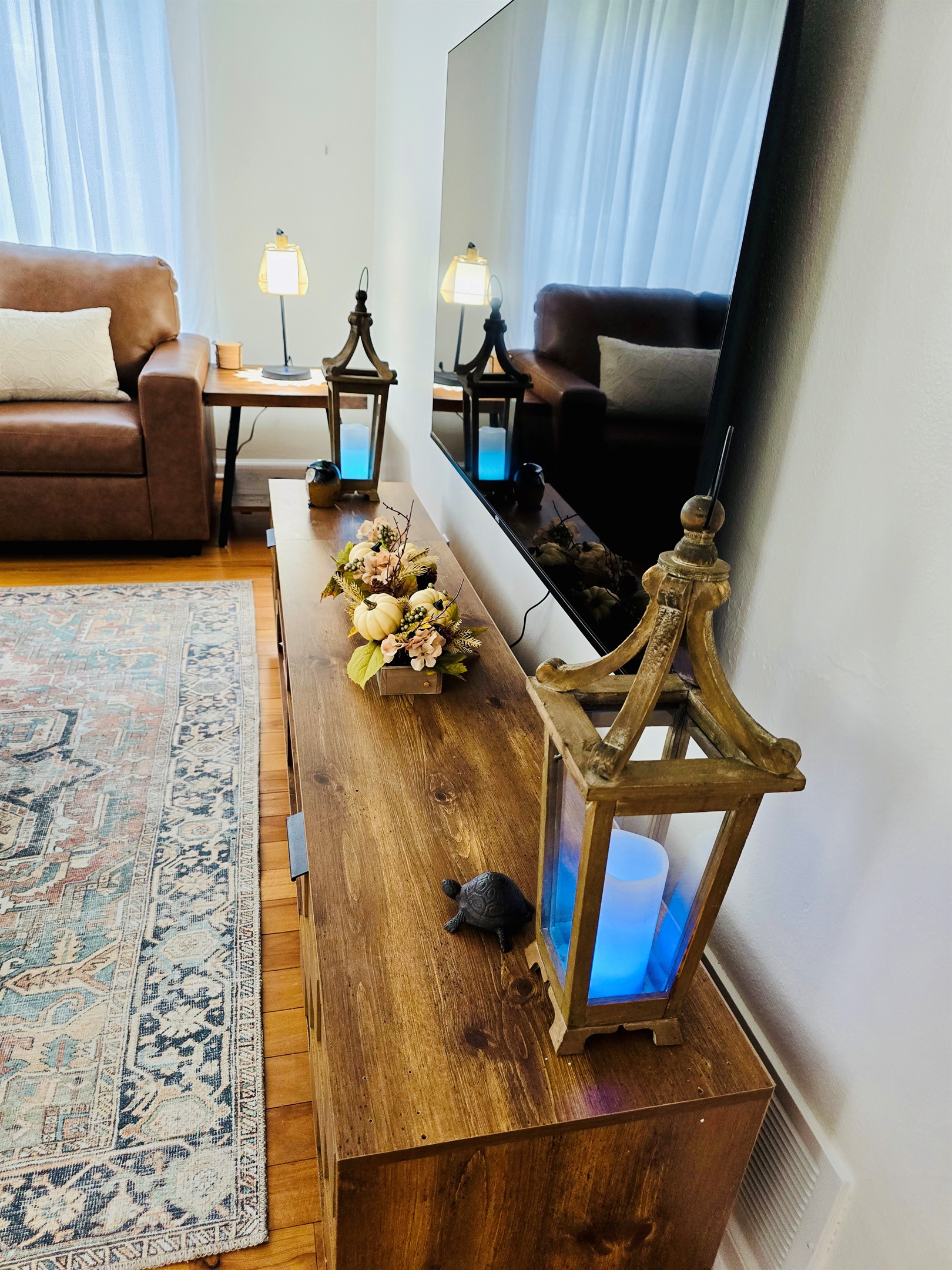 A 65\" mounted TV anchors the living room, while lanterns and flameless candles add a soft, ambient glow for cozy evenings