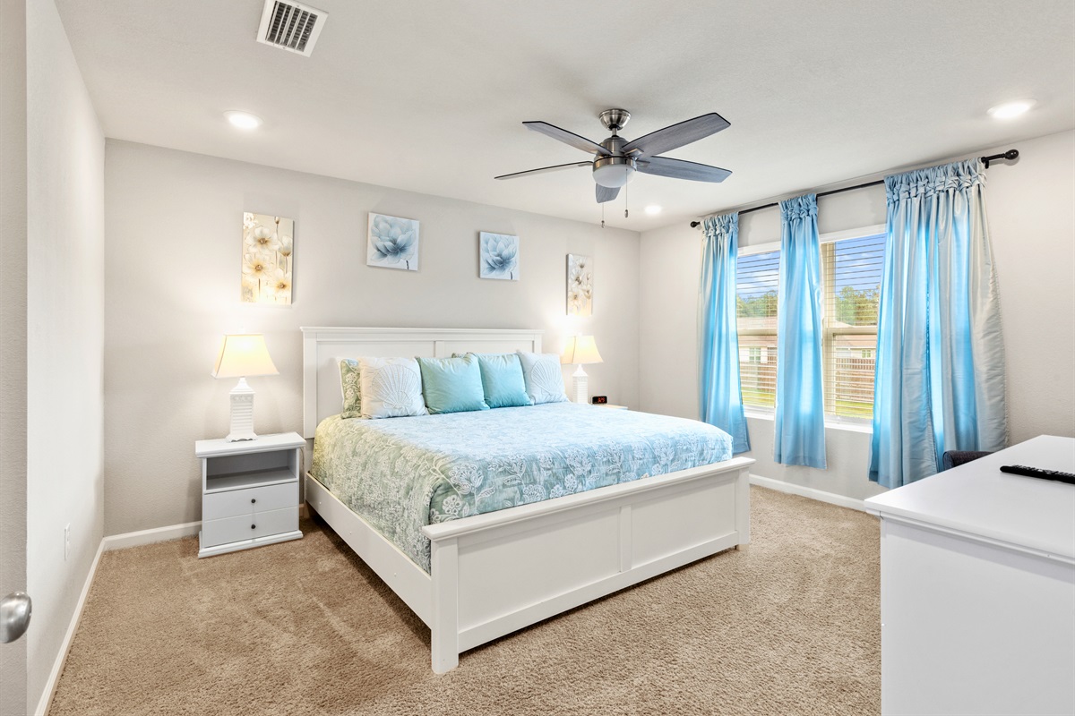 Another view of the inviting king bedroom with light, airy curtains and cozy carpet underfoot.