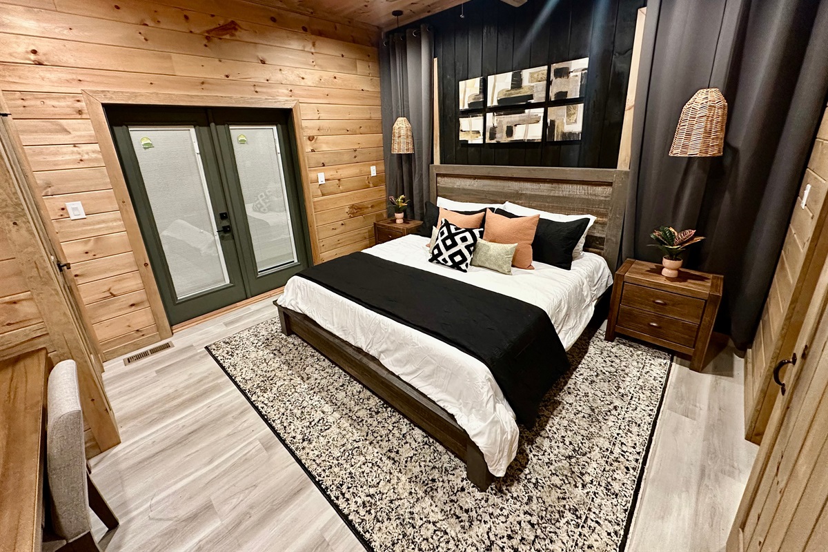 A cozy king retreat with warm wood walls, layered textures, and soft lighting. Sliding doors open to fresh mountain air, creating the perfect space for slow nights and restful mornings tucked in the trees.