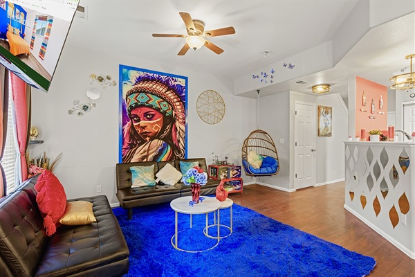 Spacious and eclectic living room with a cozy seating area, a unique hanging chair, and a vibrant Native American-inspired tapestry. Perfect for relaxing and unwinding.
