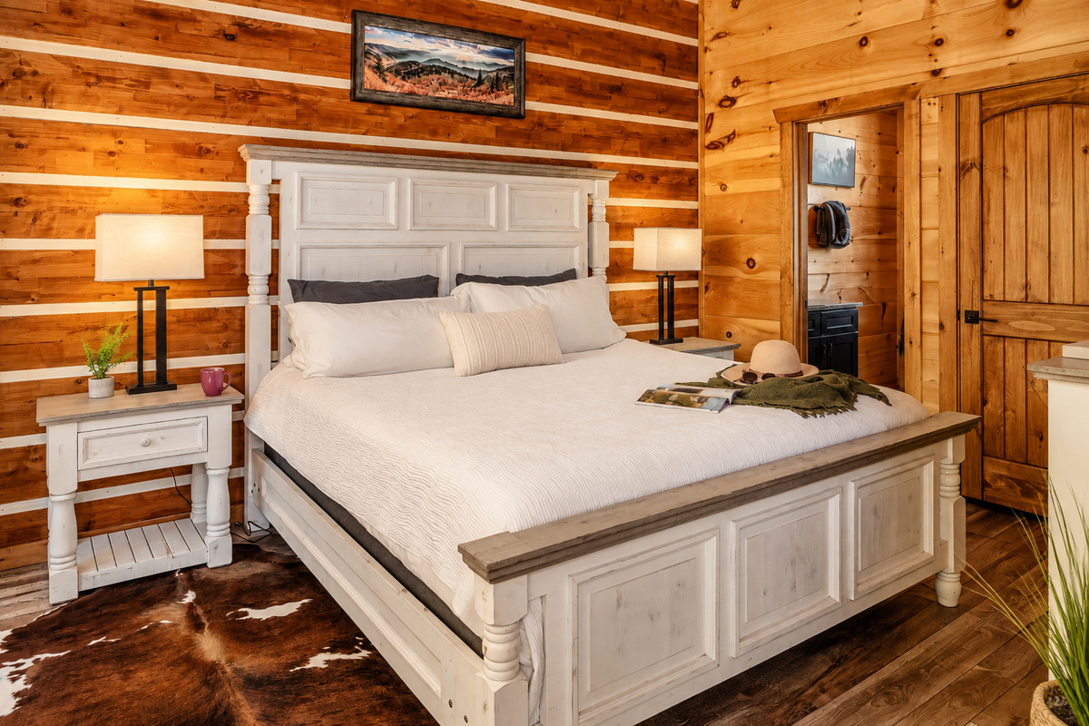 A whitewashed king bed against chinked log walls, with an en-suite bath nearby.