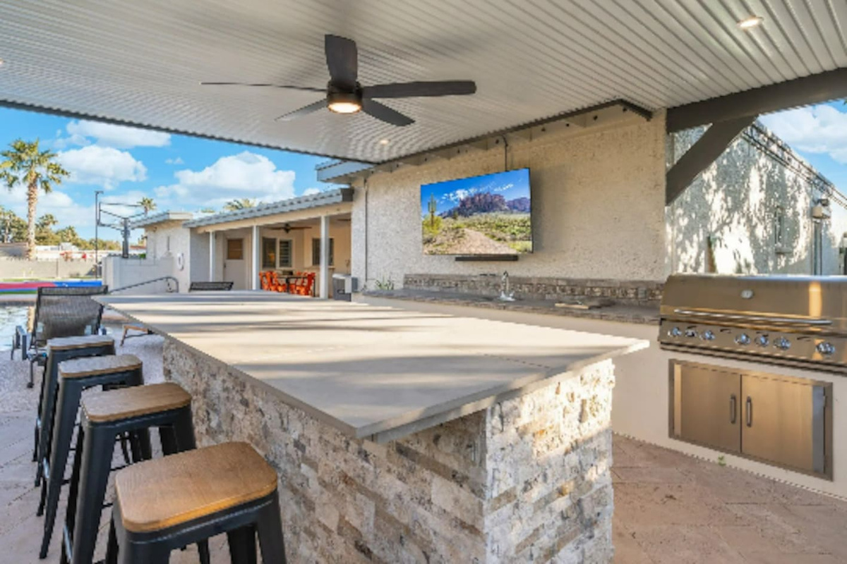 Bar stools line the outdoor kitchen, with a mounted TV keeping the group entertained while the grill does its work.