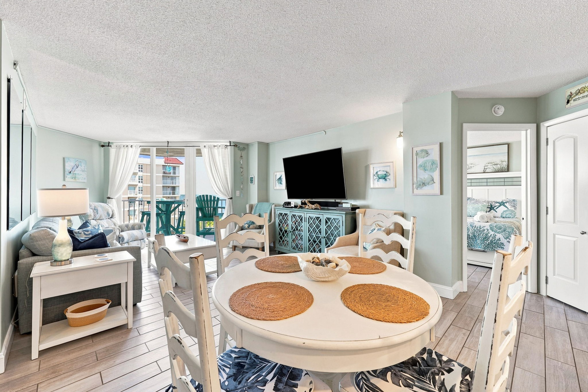 Open coastal layout connecting the dining space, living room, and sunlit balcony doors.