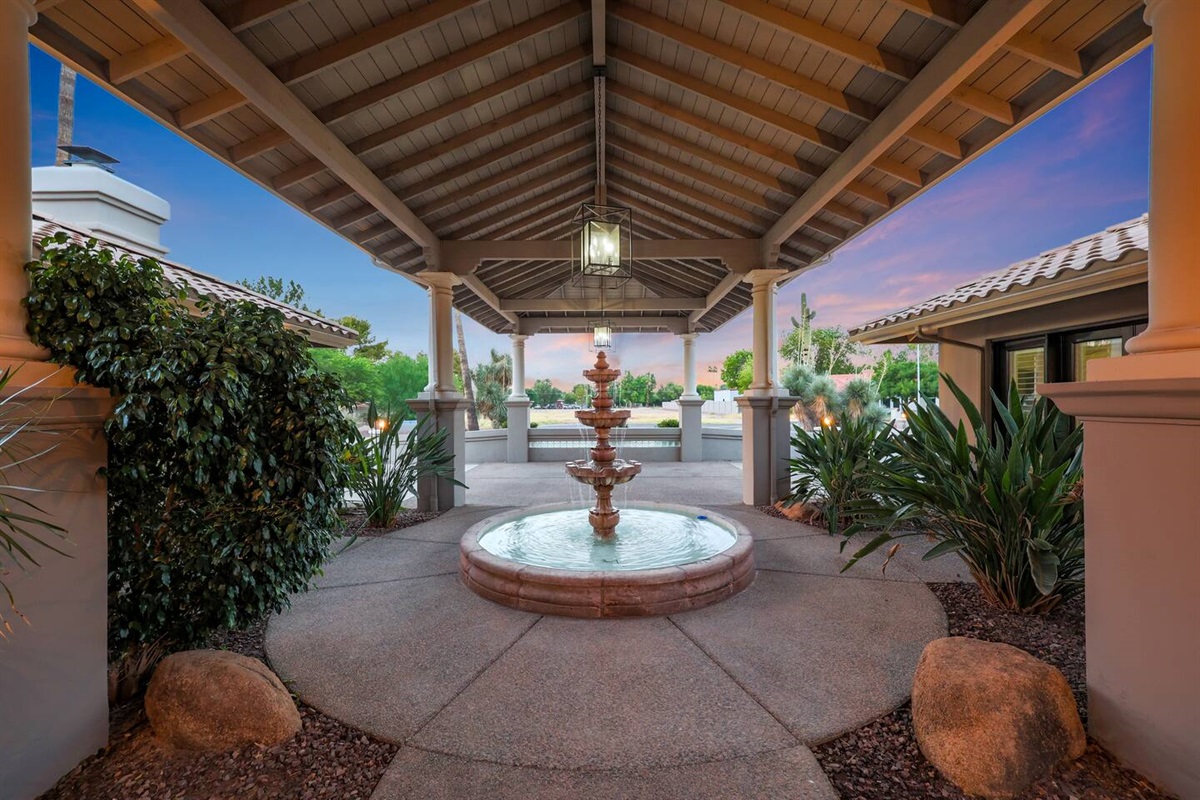 Arrive in style through this stunning covered entryway, complete with a classic multi-tiered fountain and lush landscaping.