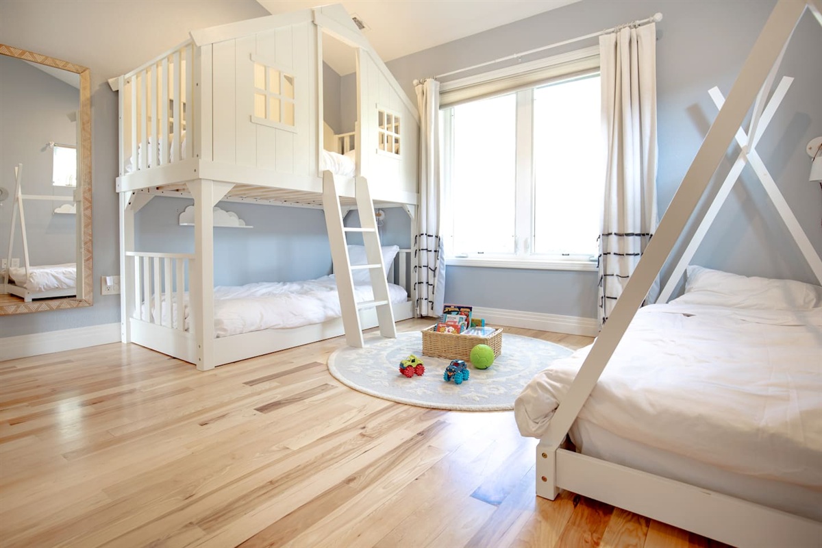 A cheerful and spacious kids’ room with a charming house-style bunk bed, a single tent bed, and plenty of natural light—perfect for little adventurers