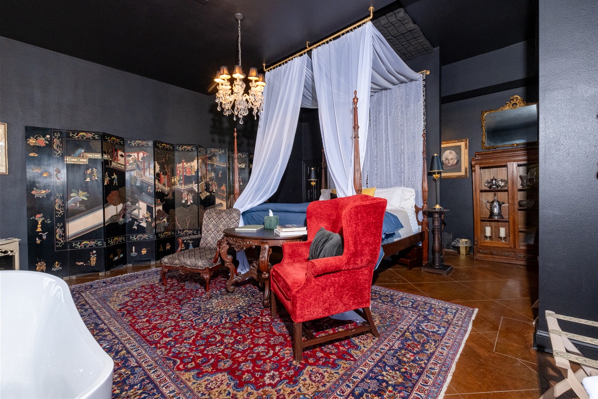 Four-poster canopy bed and seating area set beneath a crystal chandelier.