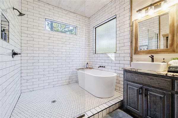 Modern rustic bathroom with a freestanding soaking tub, white subway tiles, a large window, and a sleek walk-in shower. A perfect spa-like retreat in a cozy cabin.
