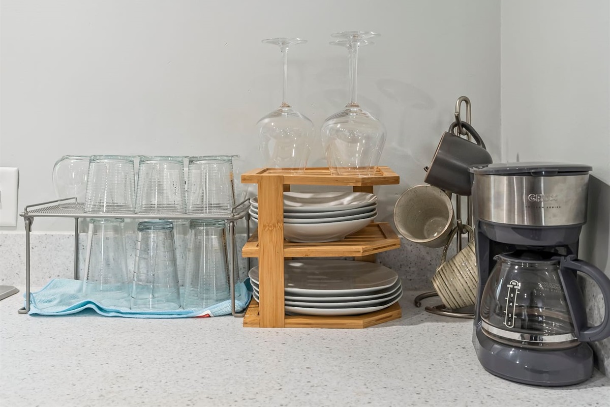 Well-organized dishware station with plates, bowls, wine glasses, and mugs neatly displayed on open shelving.