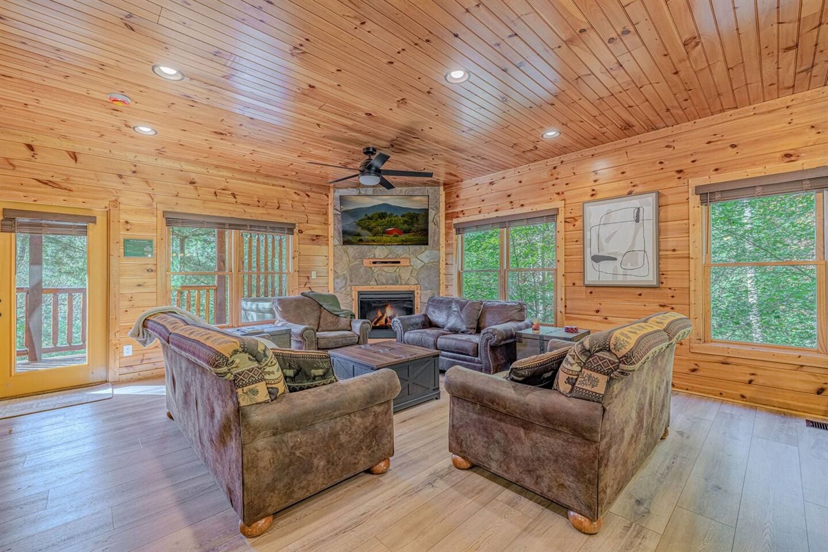 Open-concept main floor with stone fireplace, wall-mounted TV, and dining area. Luxury cabin rental in Gatlinburg, TN &mdash; sleeps 12.