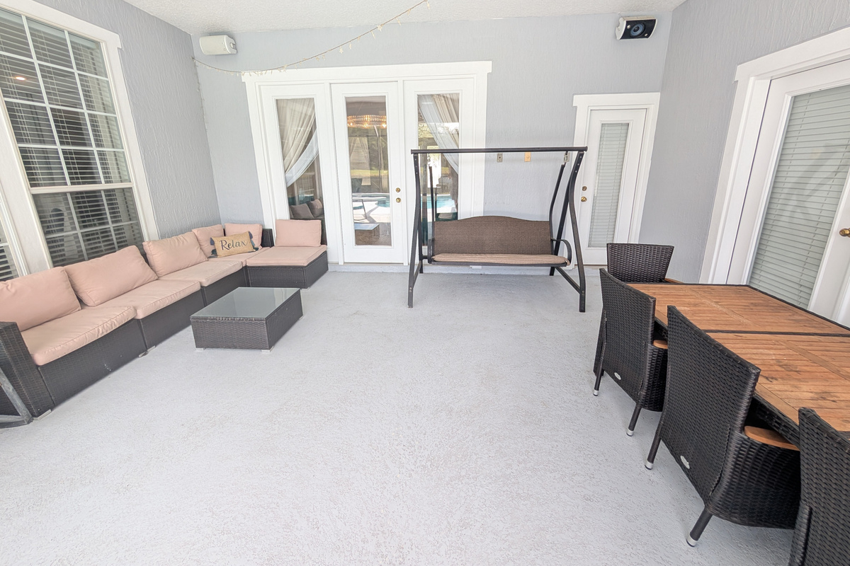 Covered outdoor living space with comfortable seating, a porch swing, and dining area just steps from the pool.
