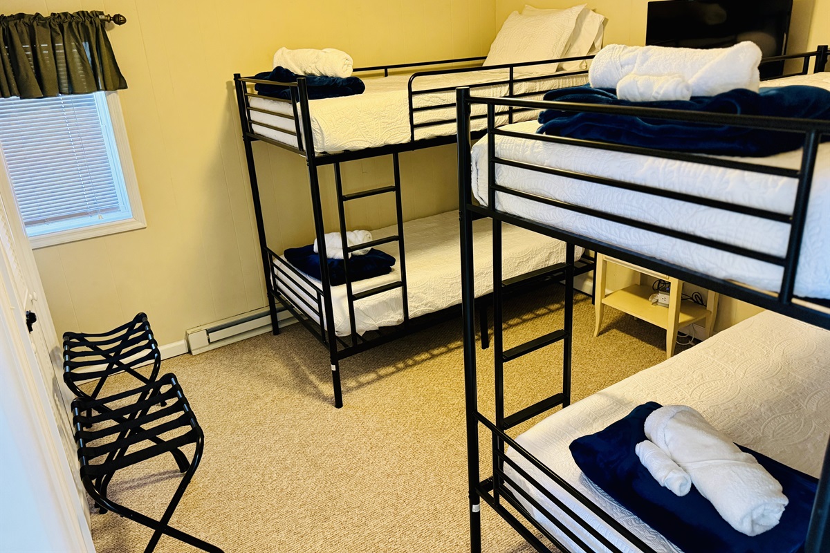 Lower Level Bunk Room beside the game room features 4 Twin beds, a nightstand, charging outlets with USB ports, 4 luggage racks, a closet to hang clothes, & a Roku Smart TV.