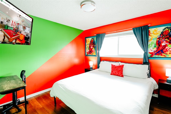 Chic Comfort: White Bed with a Splash of Orange, Bluish-Green Curtains, and Harmonious Green-Orange Walls. Natural Light and Entertainment Await 🍊📺