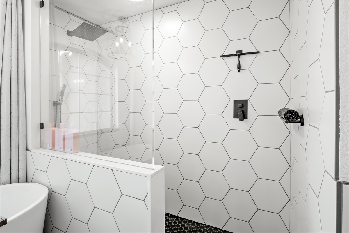 Striking walk-in shower featuring oversized hex tile, sleek black fixtures, and a rainfall showerhead for a spa-like experience. The glass enclosure keeps the space bright and open while adding a modern, high-end touch.