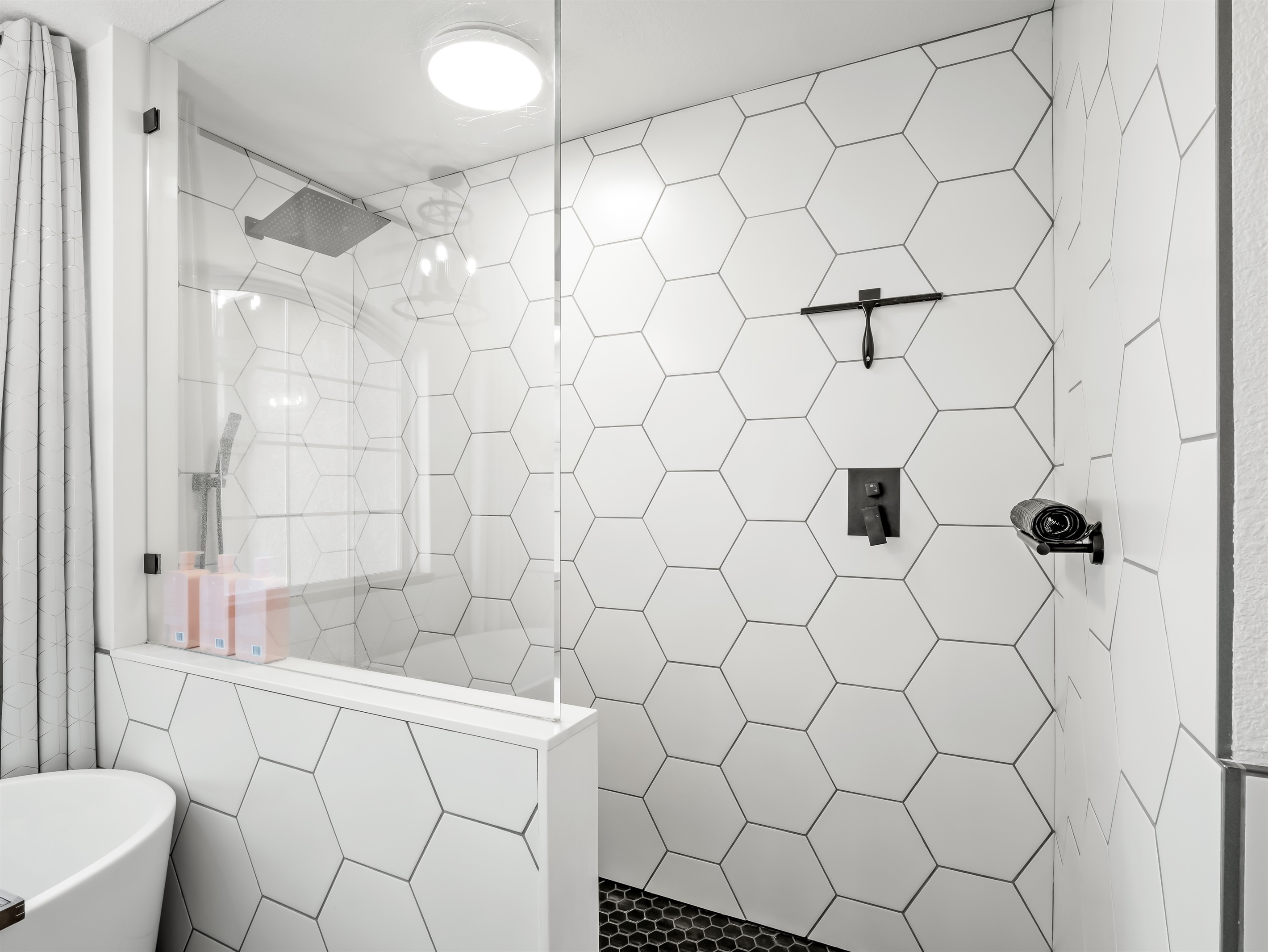 Striking walk-in shower featuring oversized hex tile, sleek black fixtures, and a rainfall showerhead for a spa-like experience. The glass enclosure keeps the space bright and open while adding a modern, high-end touch.