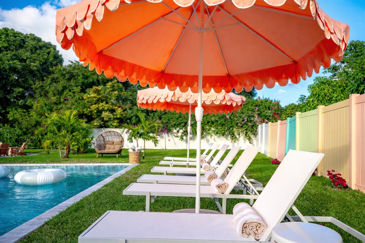 A sun-drenched Palm Beach oasis—brand-new heated saltwater pool with chic in-pool loungers, plush sunbeds, and iconic peach umbrellas, all set within a private, resort-style backyard made for long, lazy afternoons.