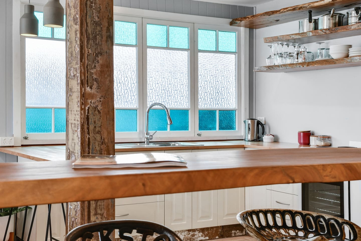 A broad timber benchtop, deep sink and open shelving give the downstairs kitchen at Aaron's Beachside Boat House a practical, character-filled workspace.