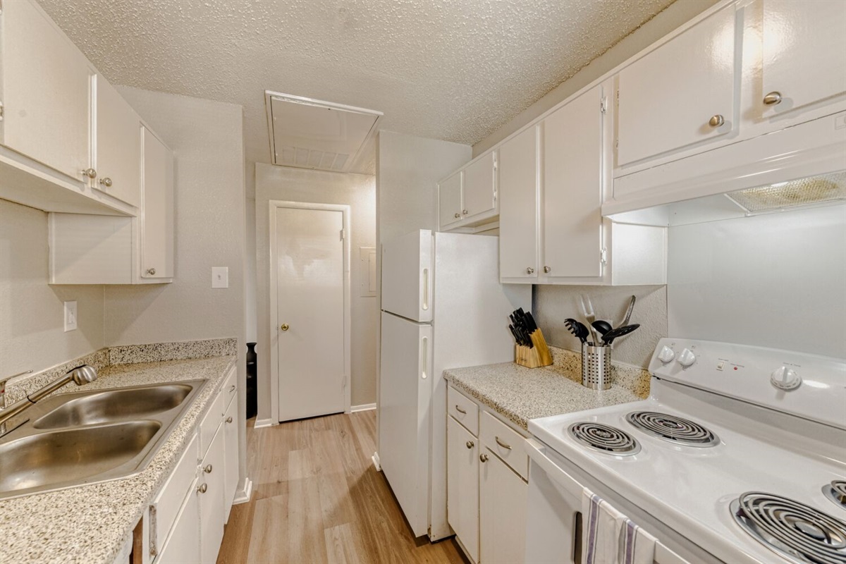 Bright galley kitchen with sleek white cabinets and warm wood flooring.