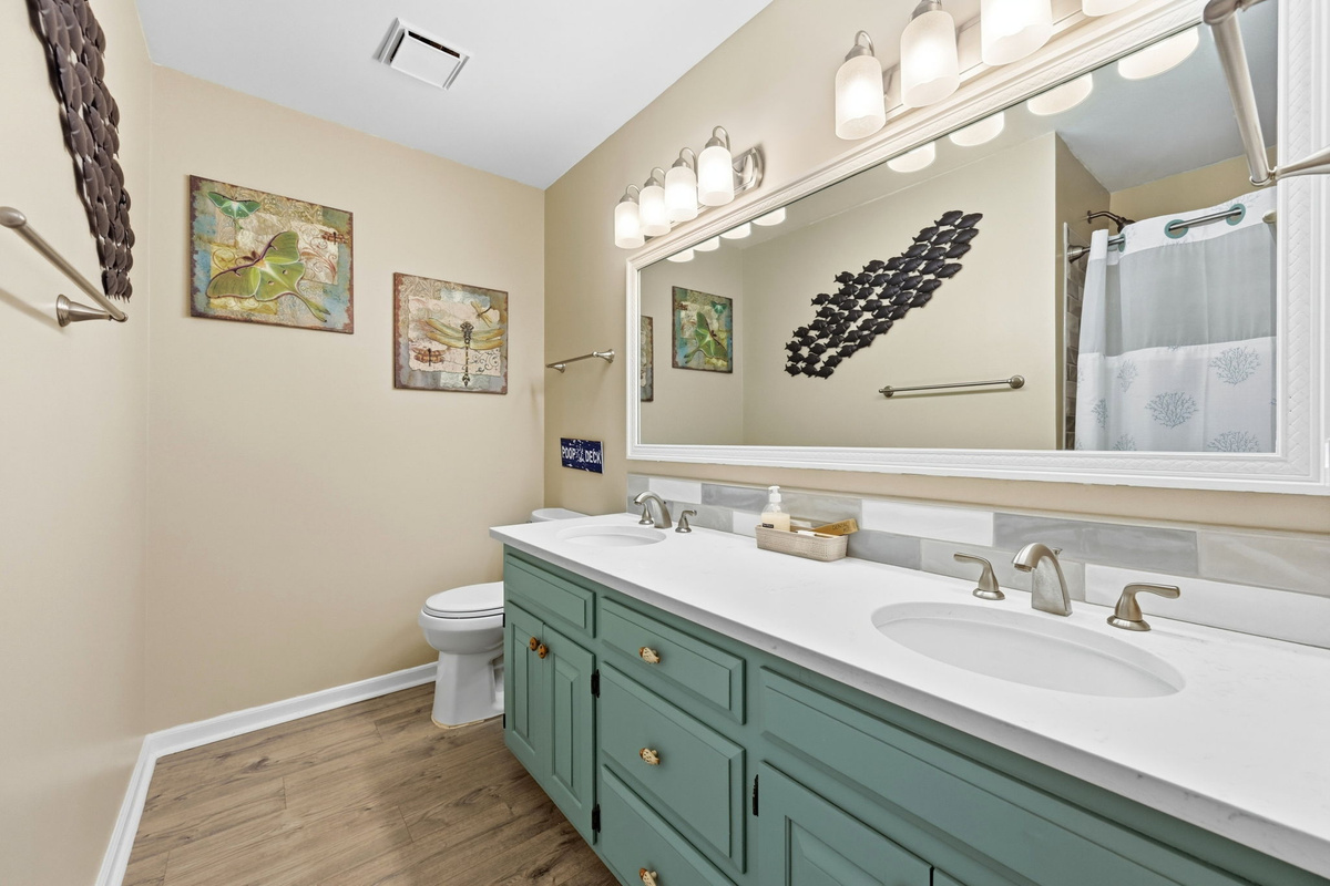 A spacious guest bathroom featuring double sinks and a convenient shower/tub combo.