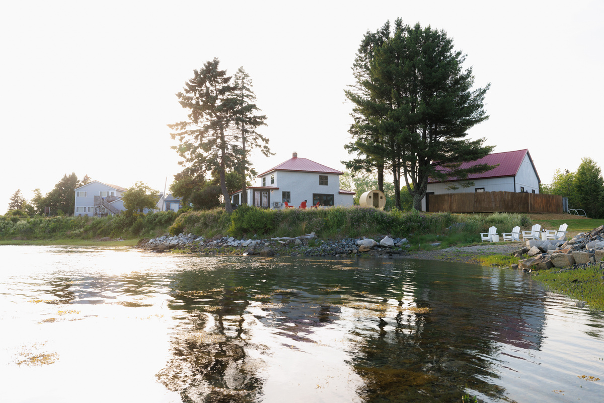 Head back to shore on the kayak and find the house glowing warm against the tree line — your retreat, the way it looks from out on the cove.