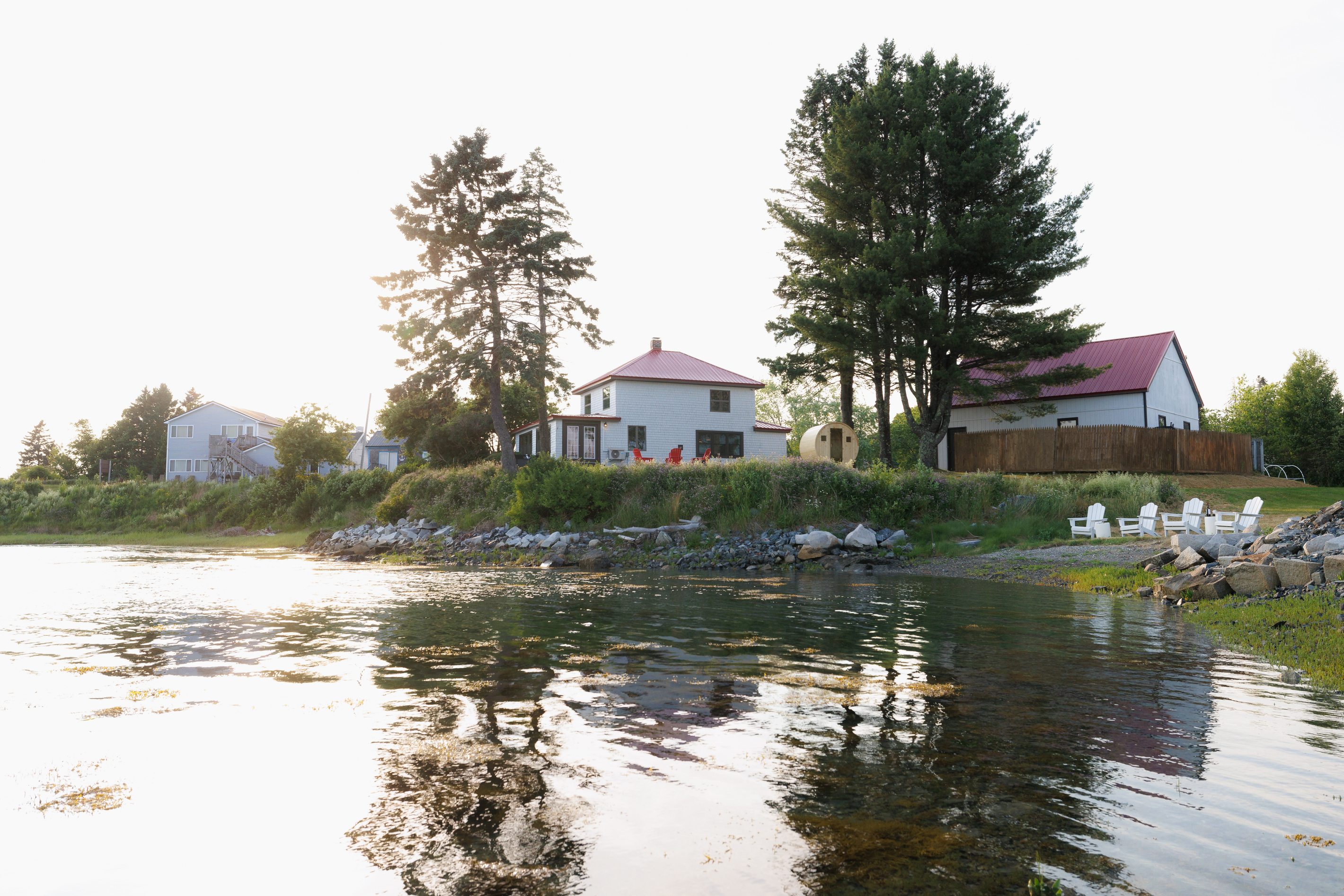 Head back to shore on the kayak and find the house glowing warm against the tree line — your retreat, the way it looks from out on the cove.